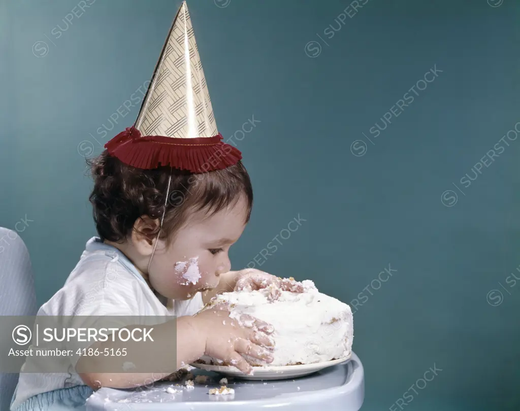 1960S Baby In Highchair Wearing Birthday Hat Eating Whole Birthday Cake