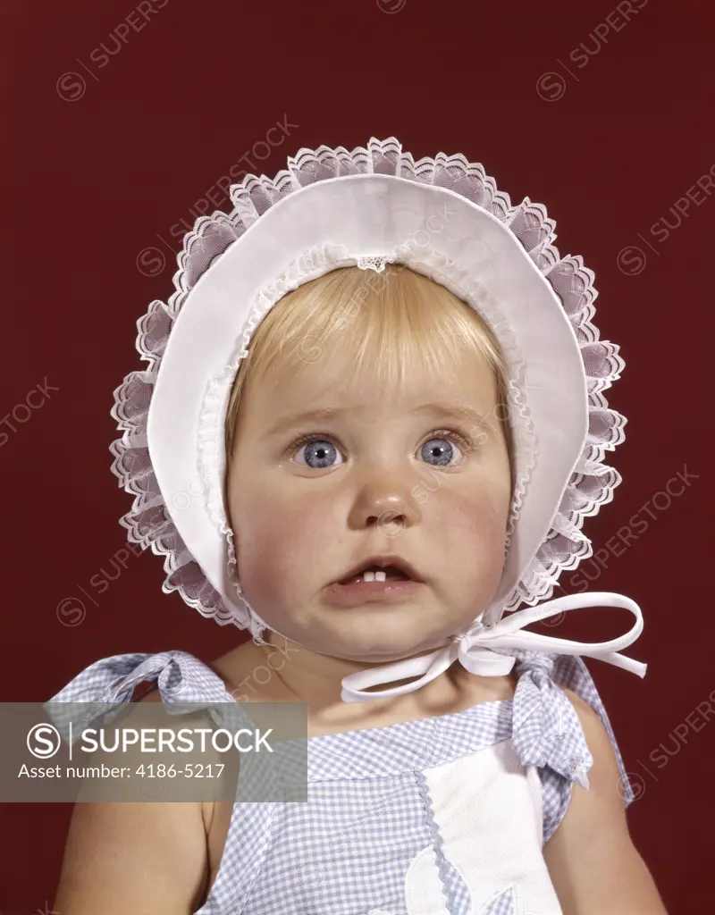 1960S Portrait Baby Girl Wearing Bonnet And Blue Gingham Dress Showing Two Front Teeth Looking At Camera