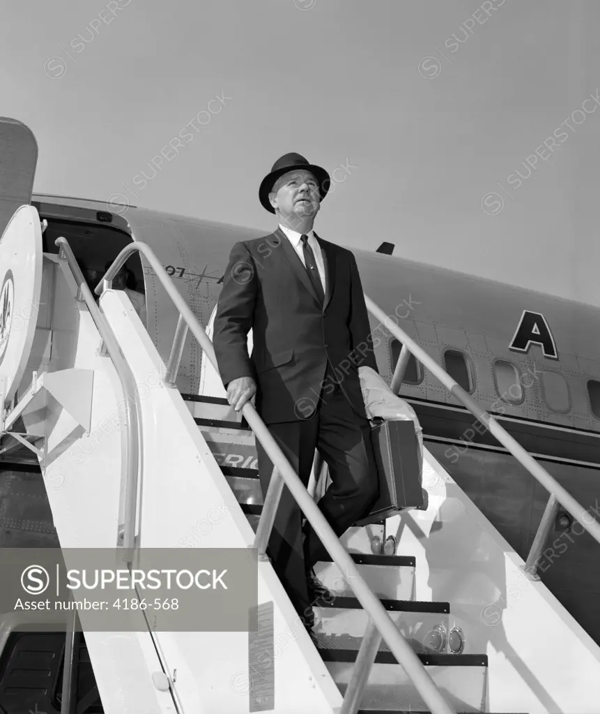 1960S Businessman Deplaning From Airplane Wearing Hat And Carrying Overcoat And Briefcase