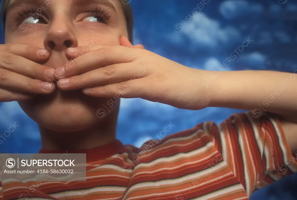 BOY WEARING STRIPED SHIRT COVERING MOUTH WITH HANDS PAINTED CLOUDS BACKDROP