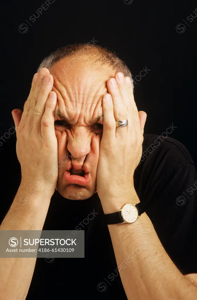 PORTRAIT OF STRESSED MAN SCRUNCHING UP FACE WITH HANDS