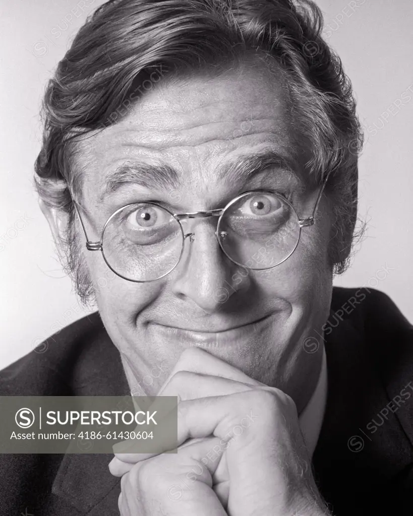 1970s PORTRAIT MAN RESTING HIS CHIN ON CLASPED HANDS SMILING WEARING ROUND METAL FRAME EYEGLASSES FUNNY FACIAL EXPRESSION - p7960 HAR001 HARS SATISFACTION STUDIO SHOT COPY SPACE ASKING PERSONS MALES CHIN CONFIDENCE EYEGLASSES EXPRESSIONS B&W RESTING WIDE EYE CONTACT BIZARRE BUG-EYED HUMOROUS STARING HAPPINESS WEIRD HEAD AND SHOULDERS CHEERFUL HIS GROTESQUE EXCITEMENT ZANY COMICAL UNCONVENTIONAL ANTICIPATION SMILES CLASPED COMEDY JOYFUL WACKY IDIOSYNCRATIC WIDE-EYED AMUSING EAGER ECCENTRIC GRIN MID-ADULT MID-ADULT MAN QUESTIONING STARTLED WIRE FRAME BLACK AND WHITE CAUCASIAN ETHNICITY ERRATIC