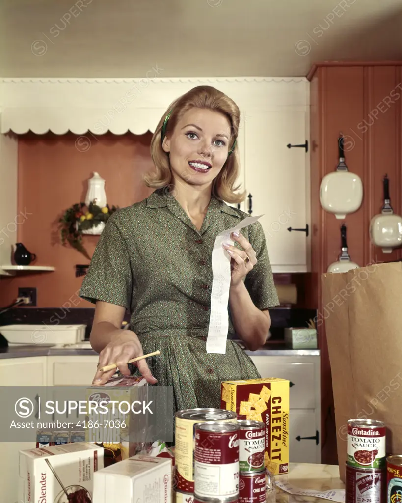 1960S Young Blond Housewife Smiling While Checking Grocery Shopping Receipt In Kitchen