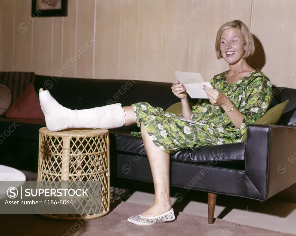 1960S Woman With Broken Leg In Cast Propped On Hamper Looking At Letter Happy Insurance Payment Basket Smiling