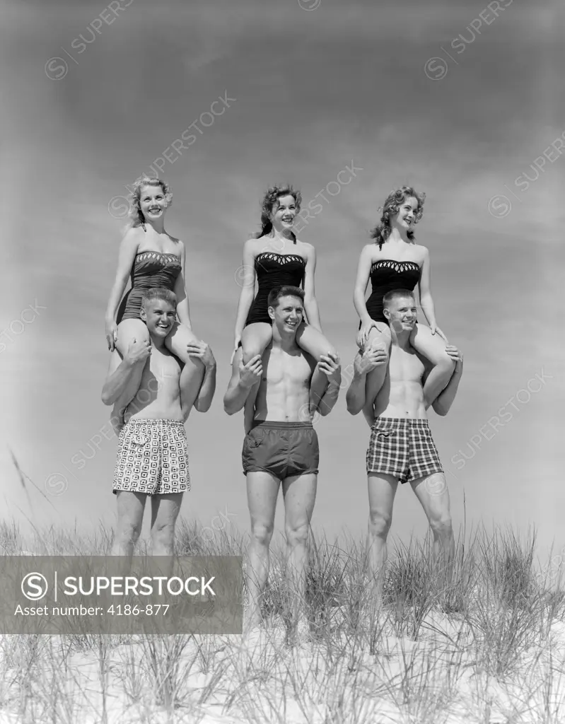 1950S 1960S Three Couples At Beach On Dunes With Women In Identical Bathing Suits Sitting On Men'S Shoulders