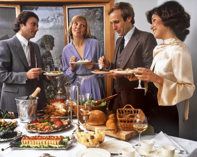 1980s MEN AND WOMEN EATING PARTY FOOD BREAD CHEESE SALADS AROUND TABLE WITH CHAMPAGNE IN ICE BUCKET