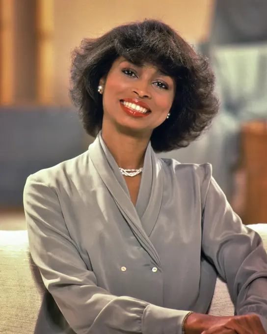 1980s AFRICAN AMERICAN BUSINESS WOMAN SMILING WEAR FASHIONABLE GRAY DRESS LOOKING AT CAMERA