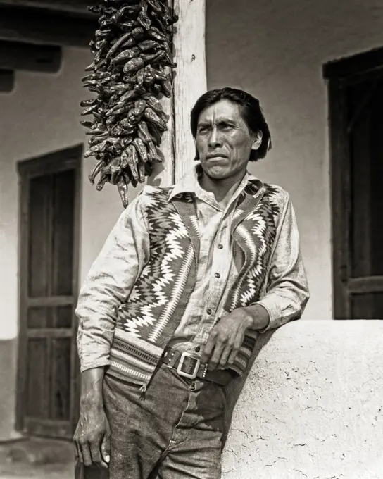 1930s PORTRAIT NATIVE AMERICAN INDIAN MAN WEARING WOVEN VEST STANDING OUTSIDE ADOBE HOME SAN ILDEFONSO PUEBLO NEW MEXICO USA