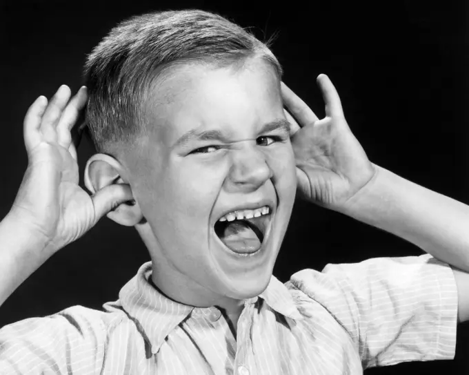 1950s BOY WAVING HANDS WITH THUMB IN EAR MOUTH OPEN TAUNTING MOCKING FACIAL EXPRESSION GESTURE SNEERING LOOKING AT CAMERA