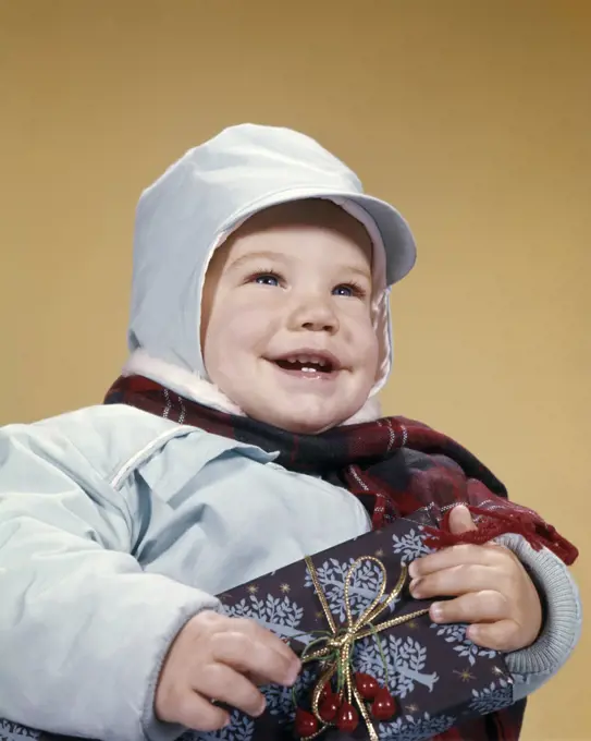 1960s SMILING TODDLER BOY WEARING WINTER SNOWSUIT HOLDING WRAPPED CHRISTMAS GIFT