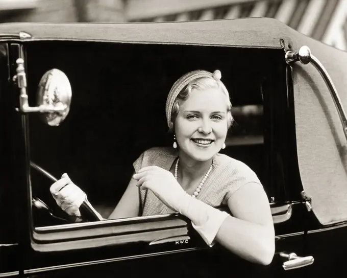 1920S 1930s SMILING WOMAN DRIVING CAR LOOKING OUT WINDOW WEARING GLOVES PEARL NECKLACE ELEGANTLY DRESSED