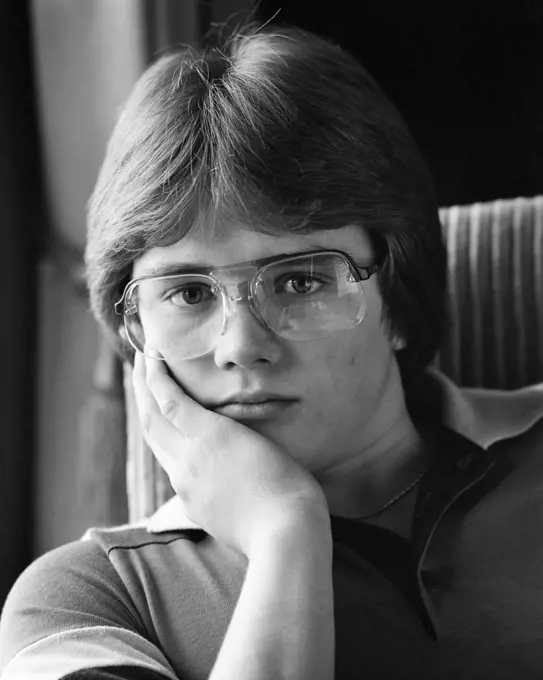 1980s PORTRAIT TEEN BOY LOOKING AT CAMERA WEARING AVIATOR FRAME EYEGLASSES WITH AN UNEMOTIONAL FACIAL EXPRESSION
