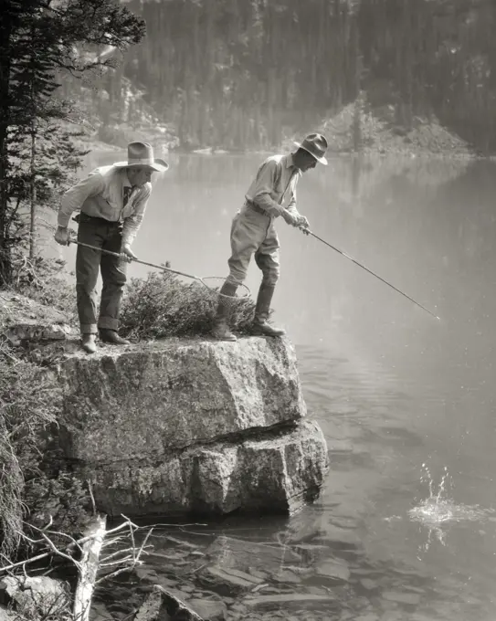 1920s TWO MEN STANDING ON ROCKY SHORE FISHING IN LAKE OHARA BRITISH COLUMBIA CANADA