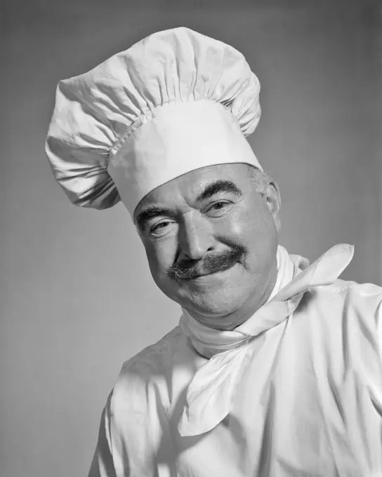 1960s SMILING MAN CHEF WITH MUSTACHE LOOKING AT CAMERA WEARING WHITE TOQUE CHEFS HAT NECKERCHIEF AND LINEN UNIFORM JACKET