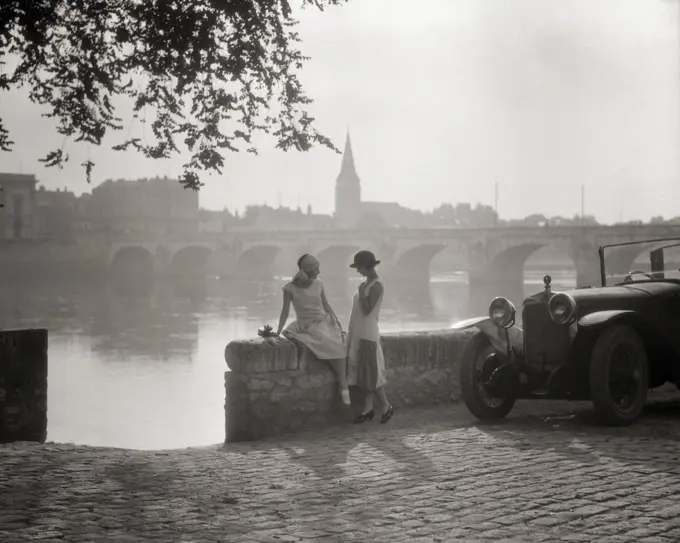 1920s TWO YOUNG WOMEN WITH ANTIQUE AUTOMOBILE SITTING STANDING TOGETHER TALKING BY STONE WALL LOIRE RIVER VALLEY FRANCE