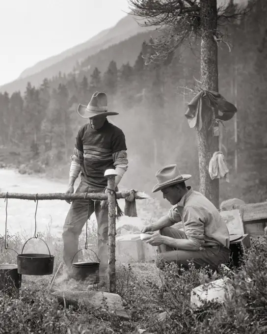 1920s 1930s TWO MEN DUDE RANCH TRAIL GUIDE COWBOYS TOGETHER PREPARING COOKING MEAL OVER CAMPFIRE BRAZEAU RIVER ALBERTA CANADA