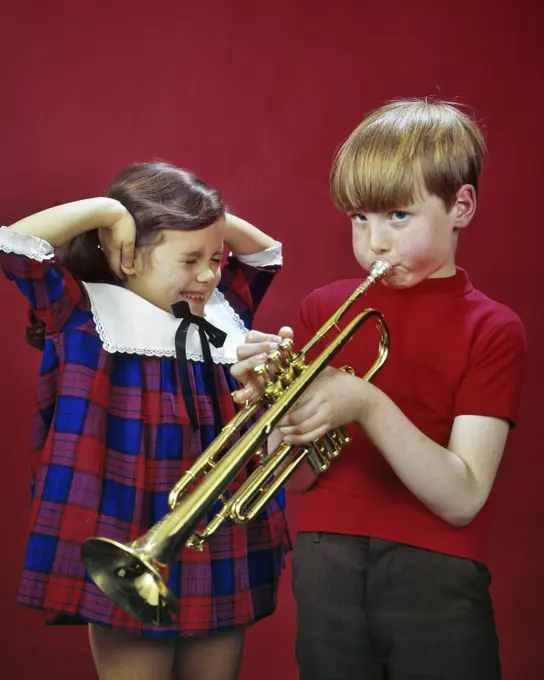 1970s 1980s LITTLE GIRL SISTER CLOSING EYES COVERING EARS HEARING LISTENING TO OLDER BOY BROTHER PRACTICING PLAYING TRUMPET