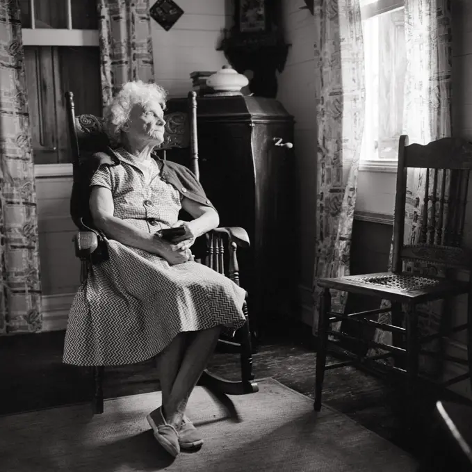 1960s SAD UNHAPPY ELDERLY WOMAN SITTING IN ANTIQUE ROCKING CHAIR LOOKING OUT THE WINDOW