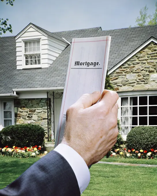 1960s MALE HAND HOLDING MORTGAGE DOCUMENT WITH SUBURBAN STONE HOUSE IN BACKGROUND