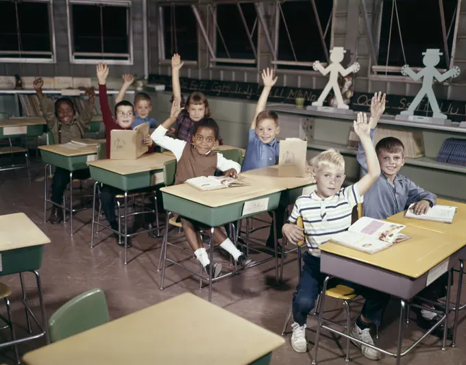 1960S Elementary School Children In Classroom With Hands Raised To Answer Question