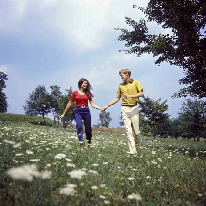 1960S 1970S Young Teen Couple Holding Hands Running Through Field Wild Flowers Queen Anne'S Lace Romance Fun Fashion