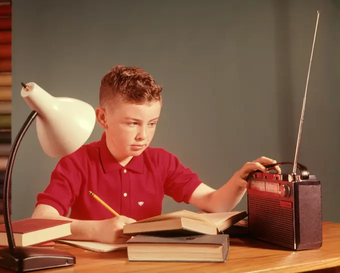 1960S Red Hair Boy Sitting At Deslistening To Portable Radio While Studying Homework  