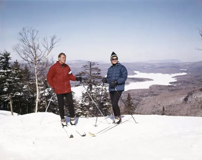 1960S Couple Man Woman Skiers Standing Top Of Hill With Vista View Winter Lake