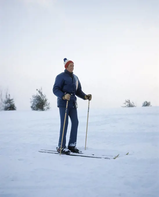 1970S Full Length Man Standing Wearing Blue Jacket Wool Cap Skis Ski Poles
