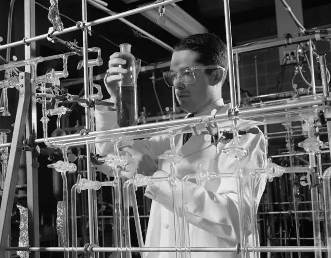 1960S Man In Lab Coat & Goggles Surrounded By Glass Tubing Conducting Scientific Research