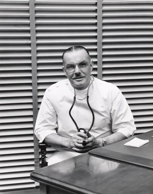 1940S Portrait Of Doctor Sitting Behind Desk Smiling