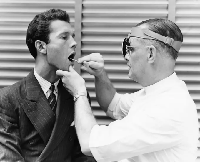 1930S 1940S Doctor Examining Throat Of Young Man Patient