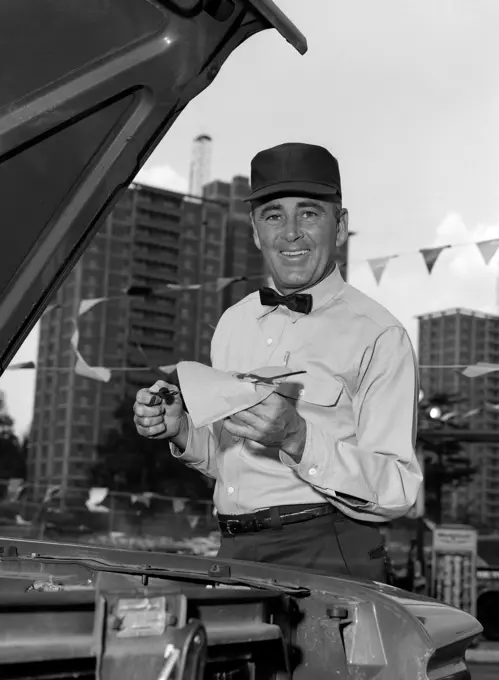 1960S Smiling Gas Station Attendant In Uniform Wiping Off Dipstick After Checking Oil