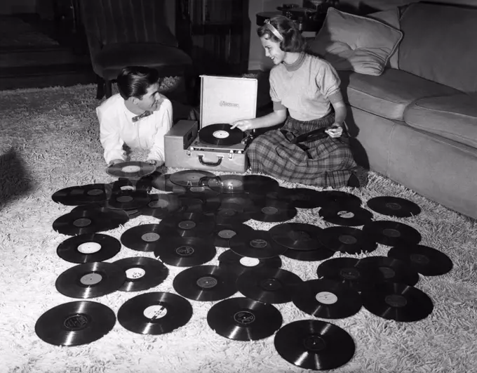 1950S Teenage Couple Playing Many Music Records Spread Out On Living Room Floor