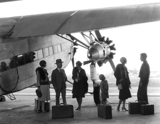 1920S 1930S Group Of Passengers Standing Under Wing Of Ford Tri-Motor Airplane With Baggage