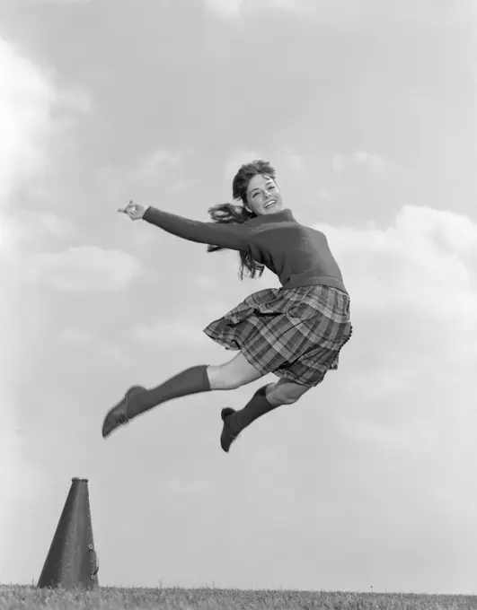 1960S Cheerleader In Sweater Plaid Skirt & Knee Socks Leaping High In Air