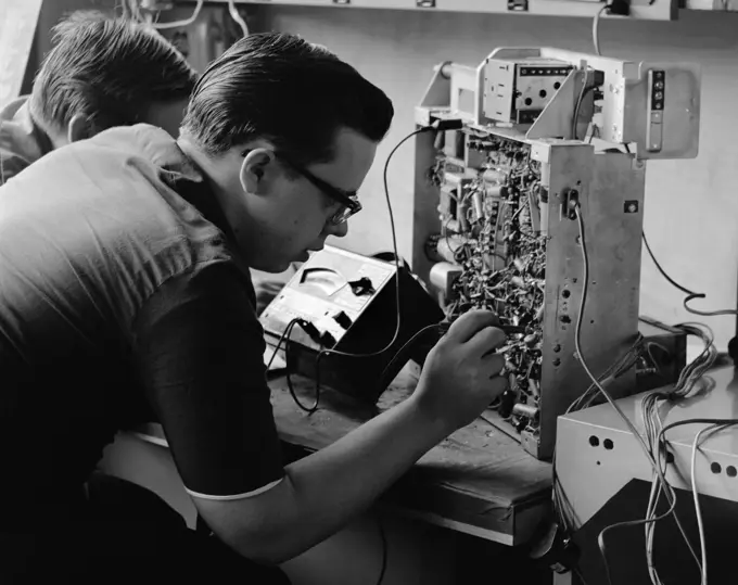 1960S Side View Of Students Working On Circuitry Panel With Small Soldering Iron