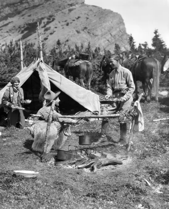 1920S 1930S Two Men And One Woman Eating A Meal Around A Campfire With A Tent And Horses At Baker Lake Alberta Canada