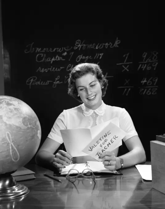 1950S Teacher Reading Valentine Card At Desk With Blackboard In Background