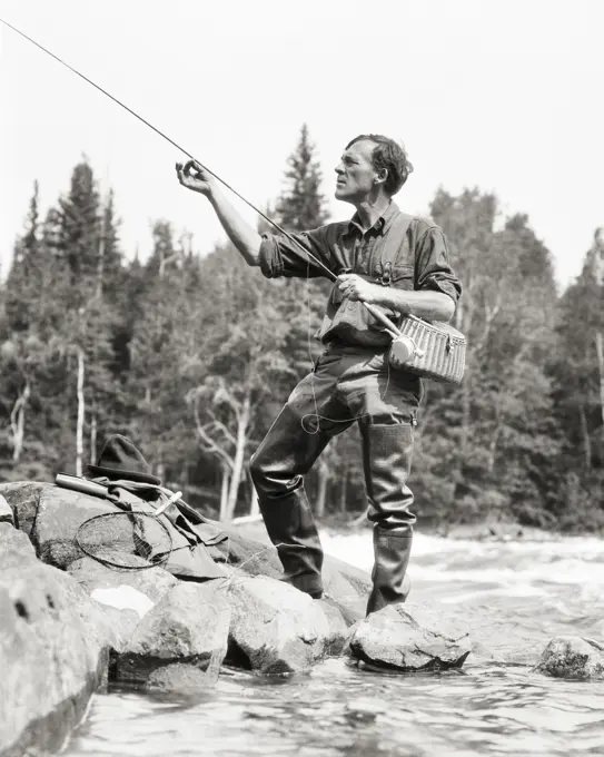 1920s FISHERMAN ADJUSTING HIS FISHING ROD BEFORE CASTING IN STREAM IN CANADA