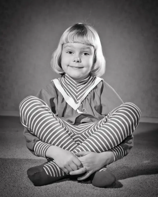 1950s 1960s SMILING BLOND GIRL QUIZZICAL FACIAL EXPRESSION SITTING CROSS LEGGED LOOKING AT CAMERA WEARING STRIPED LEOTARD TIGHTS