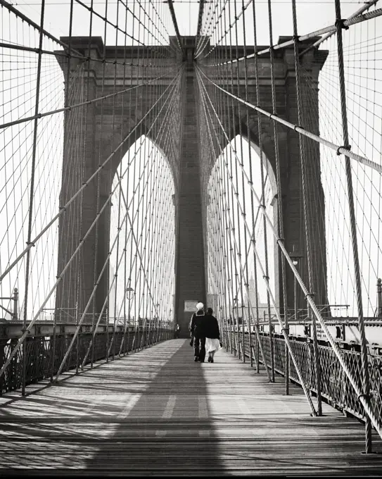 1940s BACK VIEW OF COUPLE MAN USN SAILOR IN UNIFORM WITH HIS ARM AROUND WOMAN WALKING ON THE BROOKLYN BRIDGE NEW YORK CITY USA