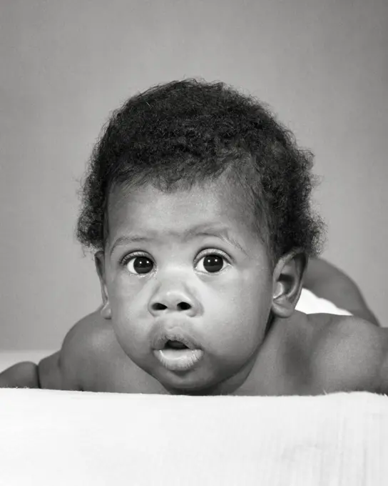 1960s AFRICAN-AMERICAN BABY LAYING ON STOMACH FUNNY FACIAL EXPRESSION