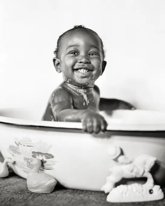 1940s SMILING AFRICAN AMERICAN BABY COVERED IN SOAPSUDS SITTING IN A BATHTUB WASH BASIN LOOKING AT CAMERA