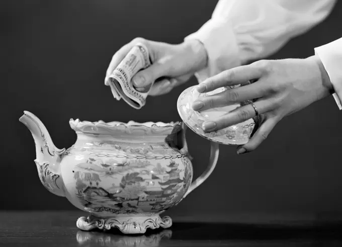 1950S Woman'S Hands Putting Wad Of Cash In Teapot