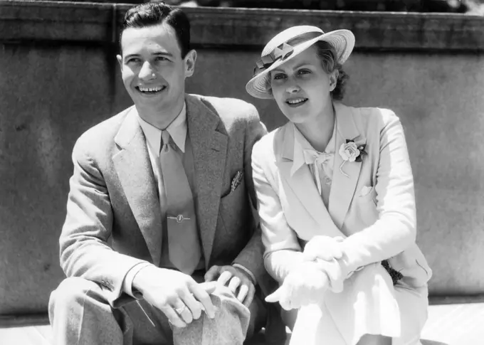 1930S Smiling Couple Sitting Outdoors In The Sunlight