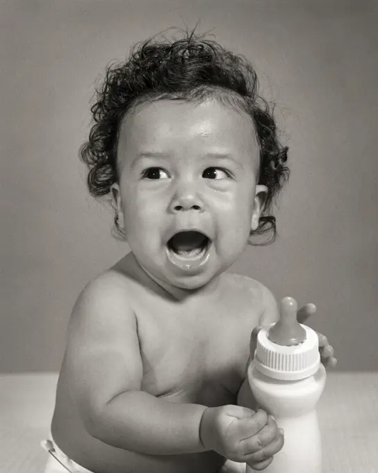 1960s SINGLE VOCALIZING AFRICAN-AMERICAN BABY BOY TODDLER SITTING HOLDING HIS OWN MILK BOTTLE 