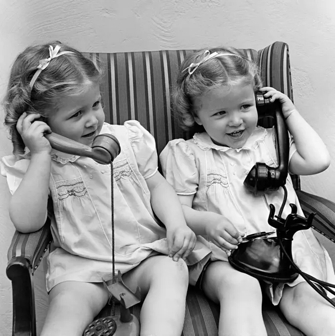 1930S 1940S Twin Little Girls Sisters Together Talking On Real And Toy Telephones Smiling Sitting Together In Chair