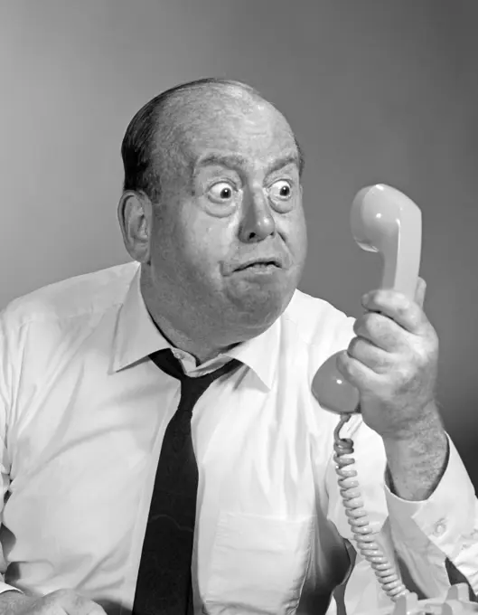 1960S 1970S Angry Balding Man Looking Bug-Eyed Into Telephone Receiver