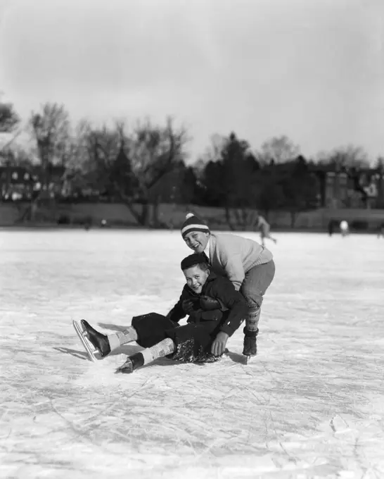 1920S 1930S Two Smiling Boys Ice Skating One Boy Fallen Other Picking Him Up