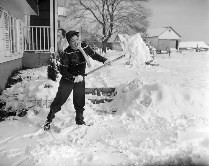 1950S Woman Struggling Working Hard Shovel Snow From Sidewalk Farm House With Porch